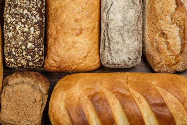 Farklı somun ekmeği ve rulo ekmeği tahtadan bir masa üzerinde un ve buğdayla.