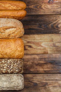 Farklı somun ekmeği ve rulo ekmeği tahtadan bir masa üzerinde un ve buğdayla.