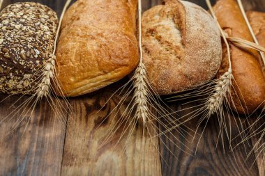 Farklı somun ekmeği ve rulo ekmeği tahtadan bir masa üzerinde un ve buğdayla.