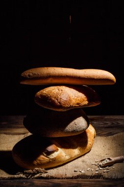 Farklı somun ekmeği ve rulo ekmeği tahtadan bir masa üzerinde un ve buğdayla.