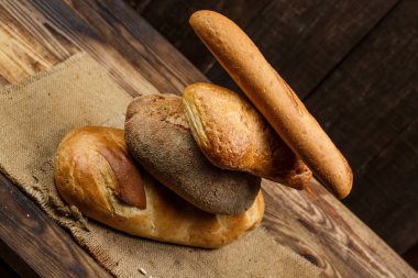 Farklı somun ekmeği ve rulo ekmeği tahtadan bir masa üzerinde un ve buğdayla.