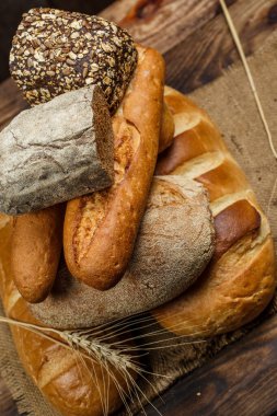 Farklı somun ekmeği ve rulo ekmeği tahtadan bir masa üzerinde un ve buğdayla.