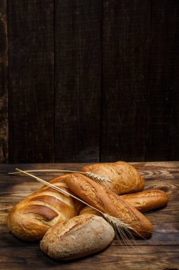 Farklı somun ekmeği ve rulo ekmeği tahtadan bir masa üzerinde un ve buğdayla.
