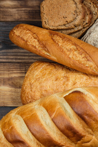 Different loaves of bread and rolls with wheat and flour on a wooden table