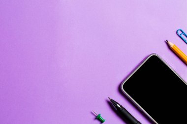 Çeşitli kırtasiye malzemeleri ve çalışma için bir telefon ve mor arka planda bir fincan kahve.