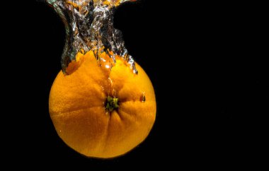 Portakallar ve buz suya düşer. Siyah arka planda sıçramalar olur..