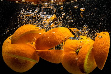 Portakallar ve buz suya düşer. Siyah arka planda sıçramalar olur..