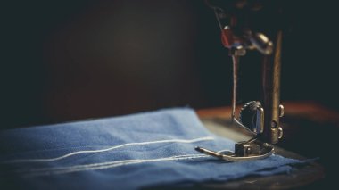 Eski dikiş makinesi, üzerine dikiş diken adam, koyu renkli.