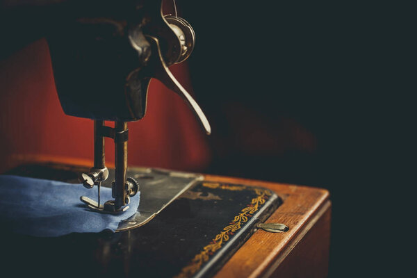 Старая швейная машинка, человек, который пришивает ее, в темных тонах
