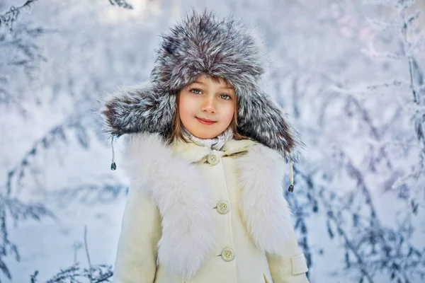 Happy adorable child girl in fur hat and coat in winter forest — Stock Photo, Image