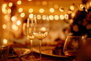 Masadaki bardaklarda şarap, arka planda ışıklar.