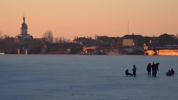 Niños caminando sobre el río congelado. El templo en el fondo, en el sol . — Vídeo de stock
