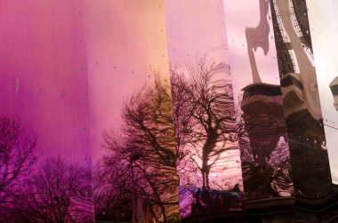 Ağaçlar ve binalar parlak metal bir duvarda yansıyor.