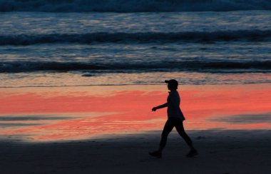 Sahile giden kişi, kırmızı su sırasında Crystal Pier yakınlarında dalgaların kenarında yürür.