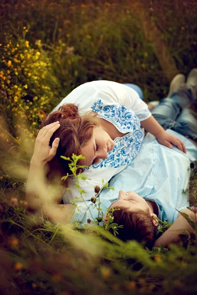 Αγάπη ζευγάρι ξαπλωμένο στο γρασίδι σε ένα πεδίο του καλοκαιριού. — Φωτογραφία Αρχείου