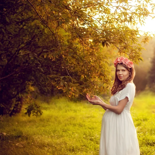 Mladá krásná těhotná žena v bílých šatech, stojící v su — Stock fotografie