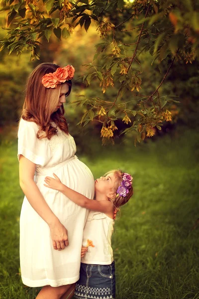 Young pregnant woman walks with her daughter. Girl hugging their — Stock Photo, Image