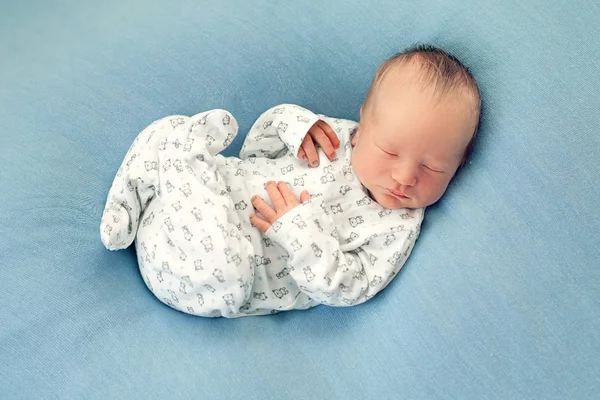 Pasgeboren jongen in slaap op een blauwe achtergrond in witte pyjama met een — Stockfoto