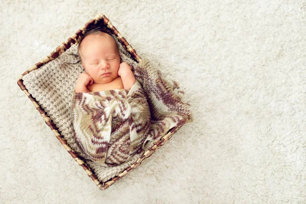 Ένα νεογέννητο μωρό που κοιμάται σε ένα συρτάρι, τυλιγμένο σε ένα πλεκτό καφέ sca — Φωτογραφία Αρχείου