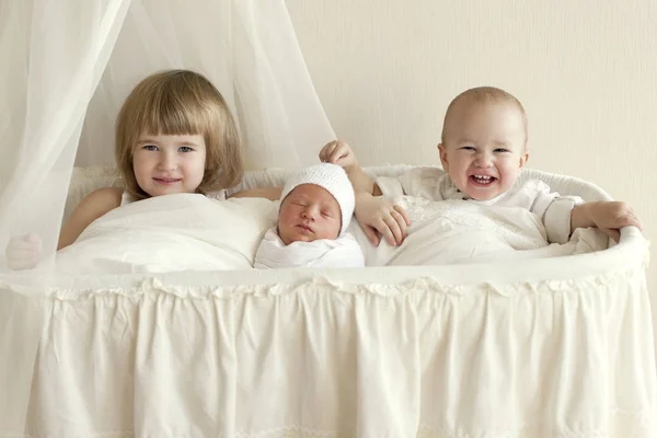 Τρία παιδιά και τα αδέλφια κάθονται σε ένα λευκό λίκνο και ένα — Φωτογραφία Αρχείου
