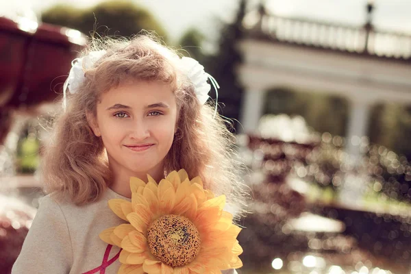 Hermosa niña de 10 años de pie cerca de una fuente, sosteniendo una — Foto de Stock