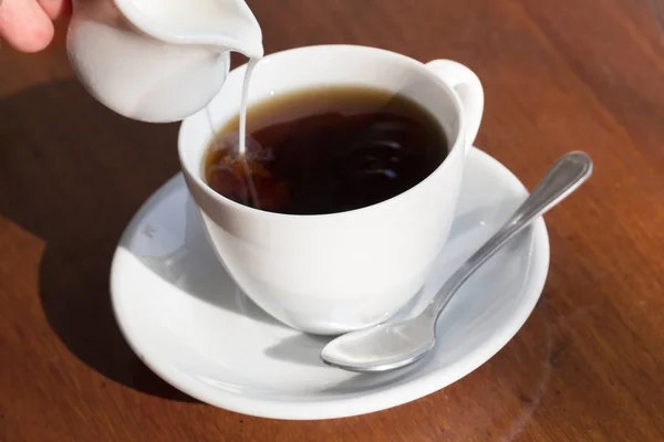 Verter leche en una taza de café negro — Foto de Stock