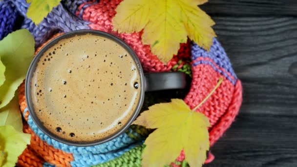 Herbst-Stillleben: eine Tasse Kaffee, umhüllt von einem warmen Strickschal, umgeben von gelben Blättern. Ansicht von oben — Stockvideo