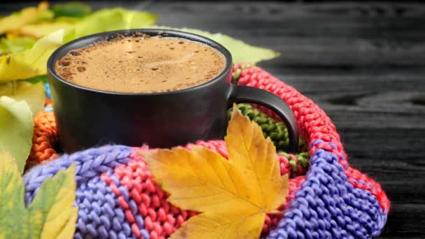 Autumn still life: a cup of coffee wrapped in a warm knitted scarf surrounded by yellow leaves. — Stock Video