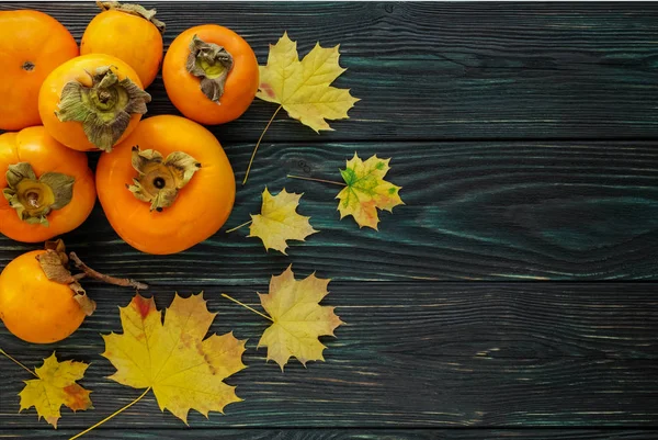 Autumn maple leaves and ripe persimmons on a wooden backgroun — Stock Photo, Image