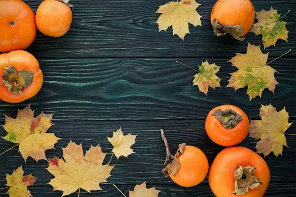 Autumn maple leaves and ripe persimmons on a wooden backgroun — Stock Photo, Image