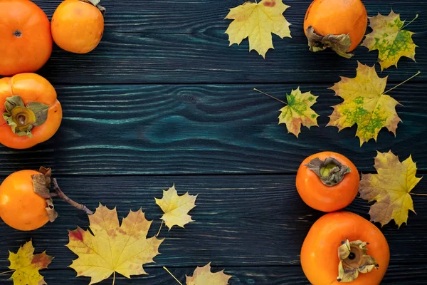 Autumn maple leaves and ripe persimmons on a wooden backgroun — Stock Photo, Image