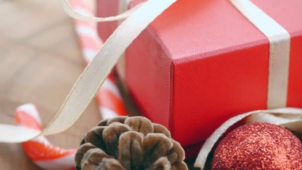 Rode geschenkdoos, dennentakken, kerstsnoep, slinger, gouden bel. Close-up. Bewegingsronde — Stockvideo