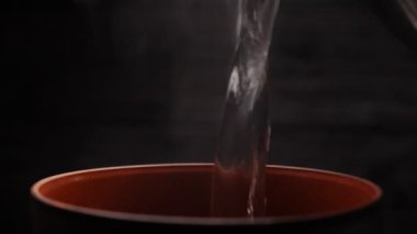 Karanlık bir arka planda kilden bir bardak. Damara sıvı döküyorum. Bir kupadan buhar çıkıyor. Damlalar. Bardaktaki hareket buharı yakın plan.