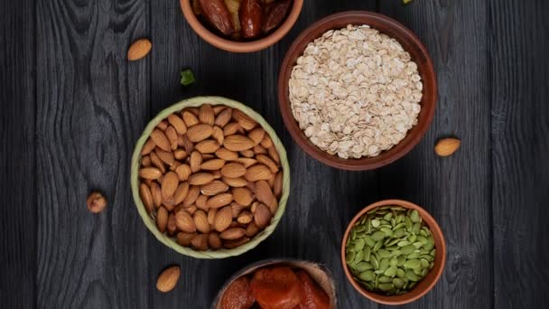 Colazione sana. Granola. Farina d'avena, fiocchi d'orzo. Noci: nocciole, mandorle, anacardi. Frutta secca: uva passa, datteri, albicocche secche. In ciotole di argilla su fondo nero, in legno. Lento motion.Vista dall'alto . — Video Stock