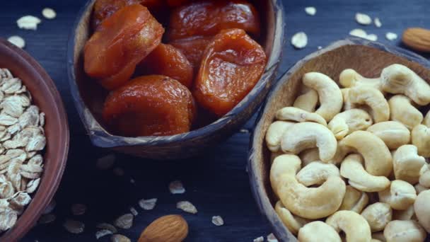 En hälsosam frukost. Granola. Havregryn, kornflingor. Nötter: hasselnötter, mandel, cashewnötter. Torkade frukter: russin, dadlar, torkade aprikoser. I lera skålar på en svart, trä bakgrund. 4k-video — Stockvideo