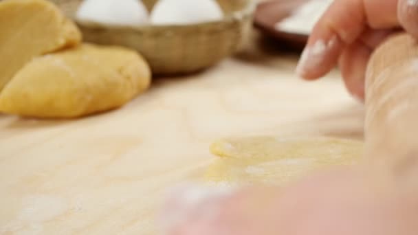 As mãos femininas rolam a massa em uma mesa de madeira, no fundo de ovos e farinha. Conceito de comida. Vídeo 4K. Movimento lento — Vídeo de Stock