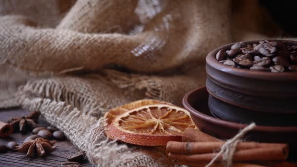 Café en grains dans une tasse d'argile, bâtonnets de cannelle, oranges séchées, morceaux de sucre sur un fond de toile de jute. Mouvement de caméra de gauche à droite. Vidéo 4k — Video