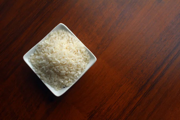 White Bowl with grains of white rice on a wooden table, top view. — Stock Photo, Image