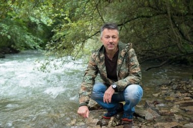 Açık sonbahar erkek portre. Mountain yakınındaki kayaların üzerinde oturan adam