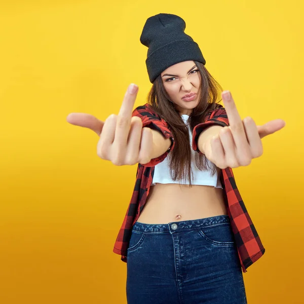 Hipster chica en jeans, camisa a cuadros y sombrero mostrando el medio f —  Fotos de Stock