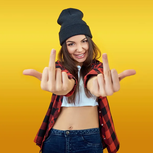 Hipster chica en jeans, camisa a cuadros y sombrero mostrando el medio f —  Fotos de Stock