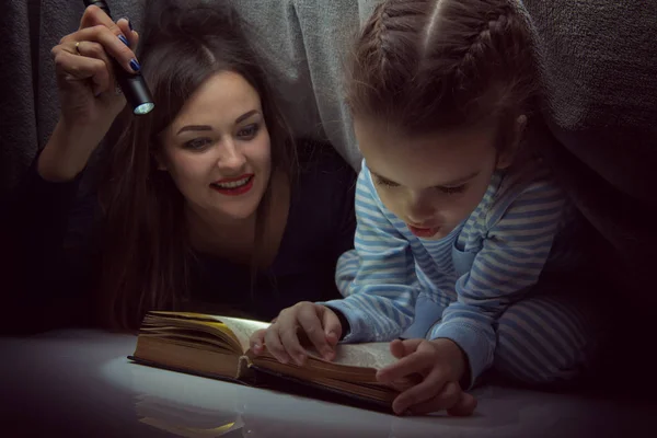 Little girl and her mother reading fairy tales book under the co