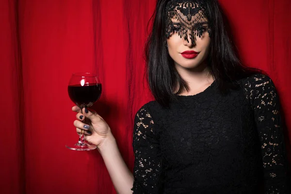 Young beautiful woman holding glass of wine over red curtains — Stock Photo, Image