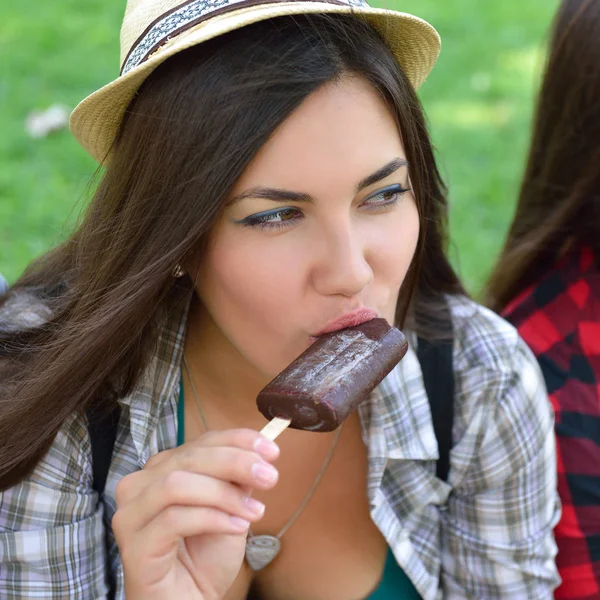 Young woman eating chocolate ice-cream outdoor in summer park. C