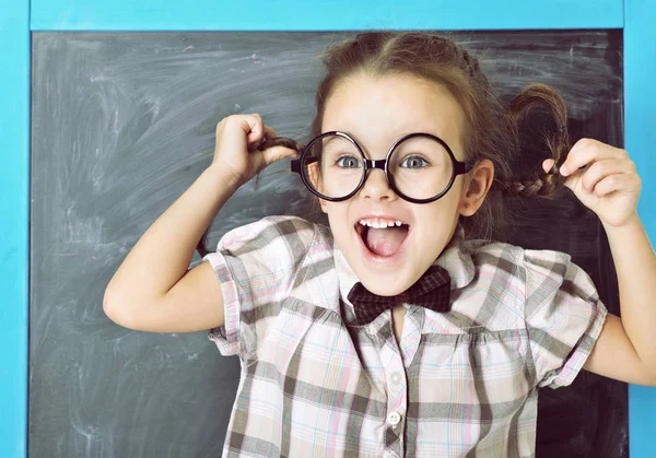 Roztomilý liitle dívka stojící poblíž tabule v legrační velkými brýlemi — Stock fotografie