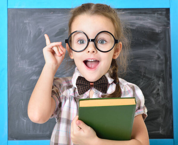 Cute liitle girl standing near blackboard in funny big glasses a