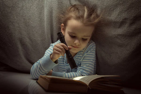 Lilla flickan läsa sagor bok under täcket på tröskeln — Stockfoto