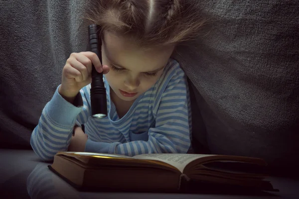 Lilla flickan läsa sagor bok under täcket på tröskeln — Stockfoto