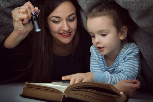 Little girl and her mother reading fairy tales book under the co