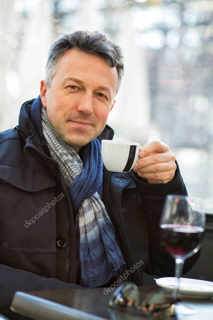 Handsome man in street winter cafe drinking coffe and wine. Male